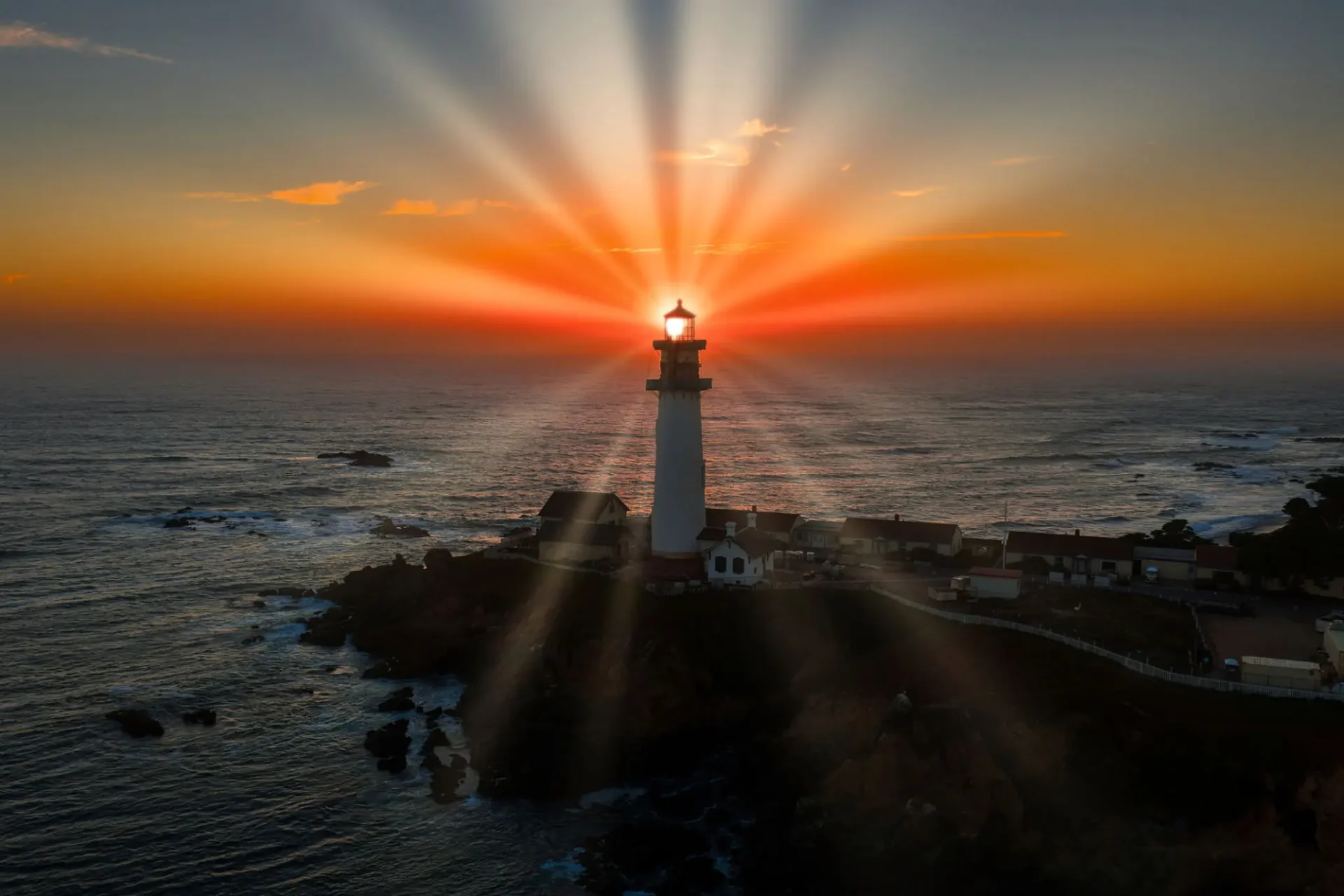 Lighthouse glowing with radiant sunbeams at sunset over the ocean.